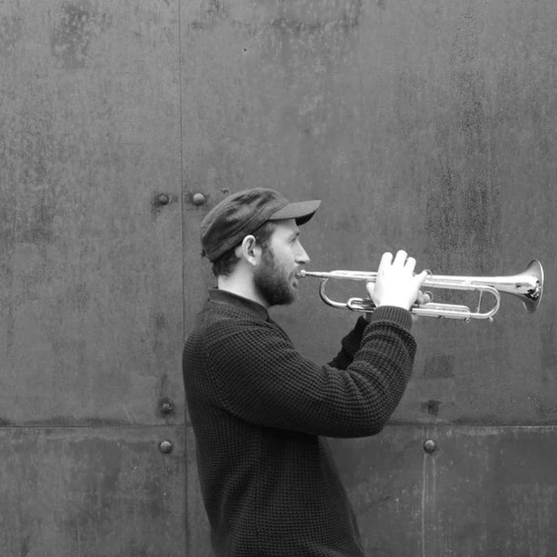 Matthew Halsall playing a trumpet against a textured wall